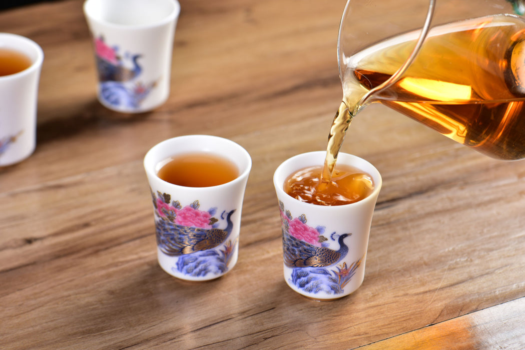 Tea being poured into a small cup with floral design on a wooden surface