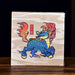 A square box containing ripe pu-erh tea with a light wood-grain background featuring a colorful illustration of a blue dragon with orange and red flames, standing on a dark wooden surface.