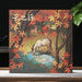 A square pu-erh tea gift box featuring a painted autumn forest scene with red and orange leaves, a white horse drinking water, and Chinese calligraphy at the top, displayed on a tabletop with a dark background and green leaves in the side.